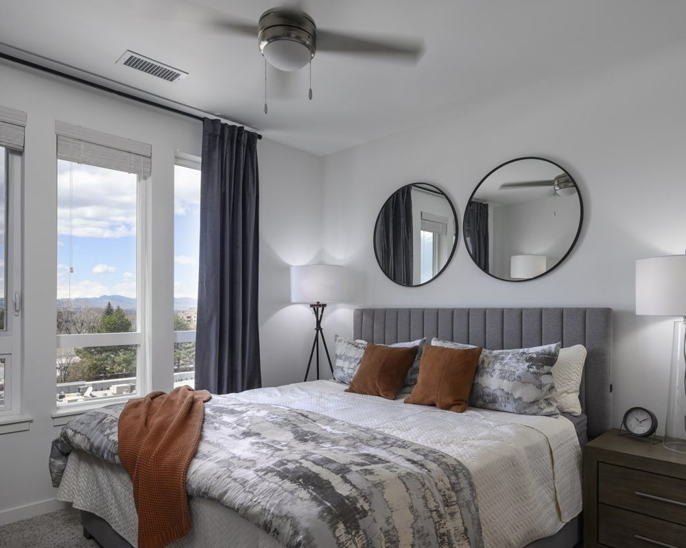 One-Bedroom Apartments in Denver, CO - Deco - Bedroom with a Ceiling Fan, Double Circle Wall Mirrors, and Modern Decor