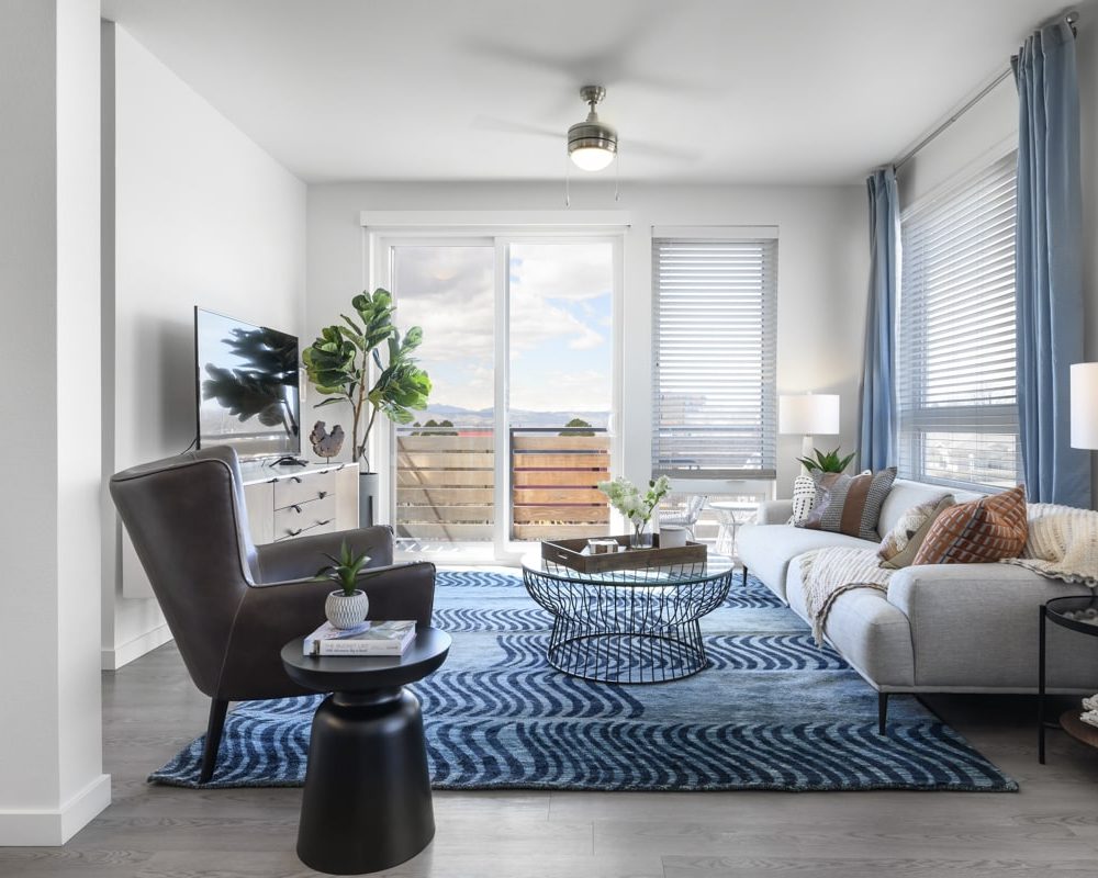 Two-Bedroom Apartments in Denver, CO - Deco - Living Room with Floor-to-Ceiling Windows, Wood-Style Floors, and a Blue Area Rug